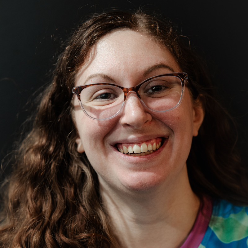 Me, a smiling curly-haired ginger with glasses, against a black background.